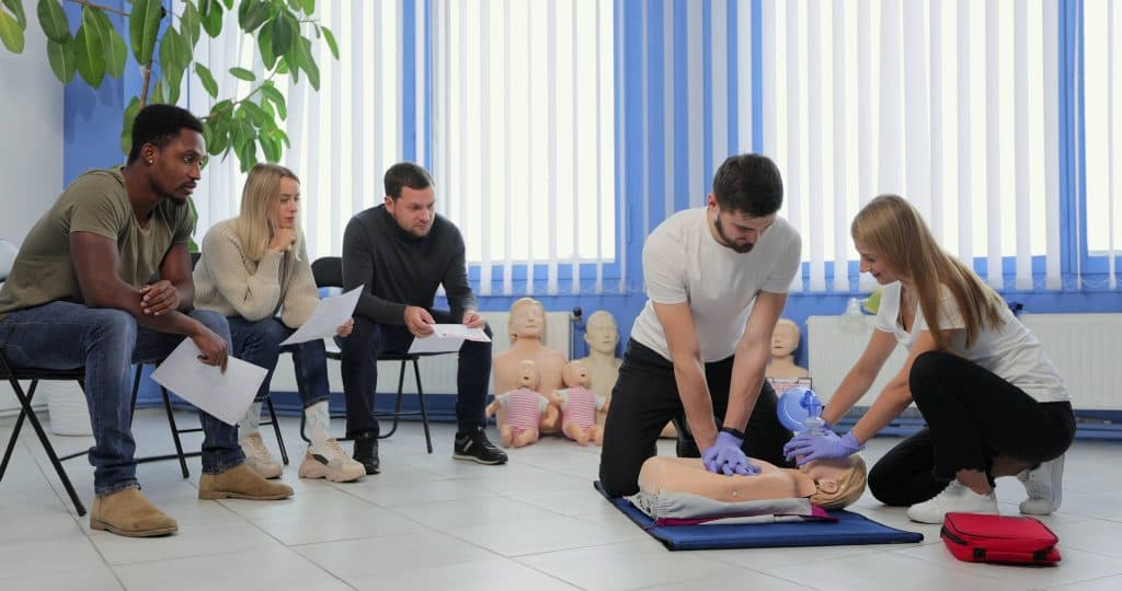 Instructors demonstrating hands-on CPR and AED training while students watch